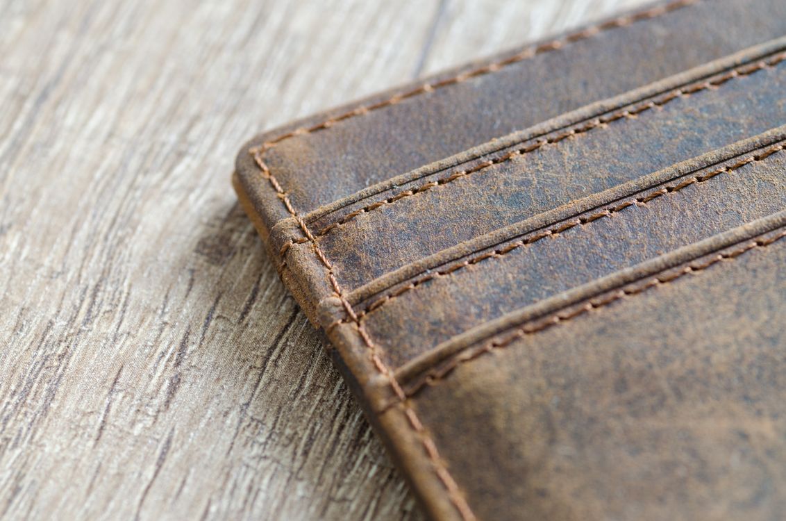 Brown leather wallet showing its surface texture and stitched edge on wood