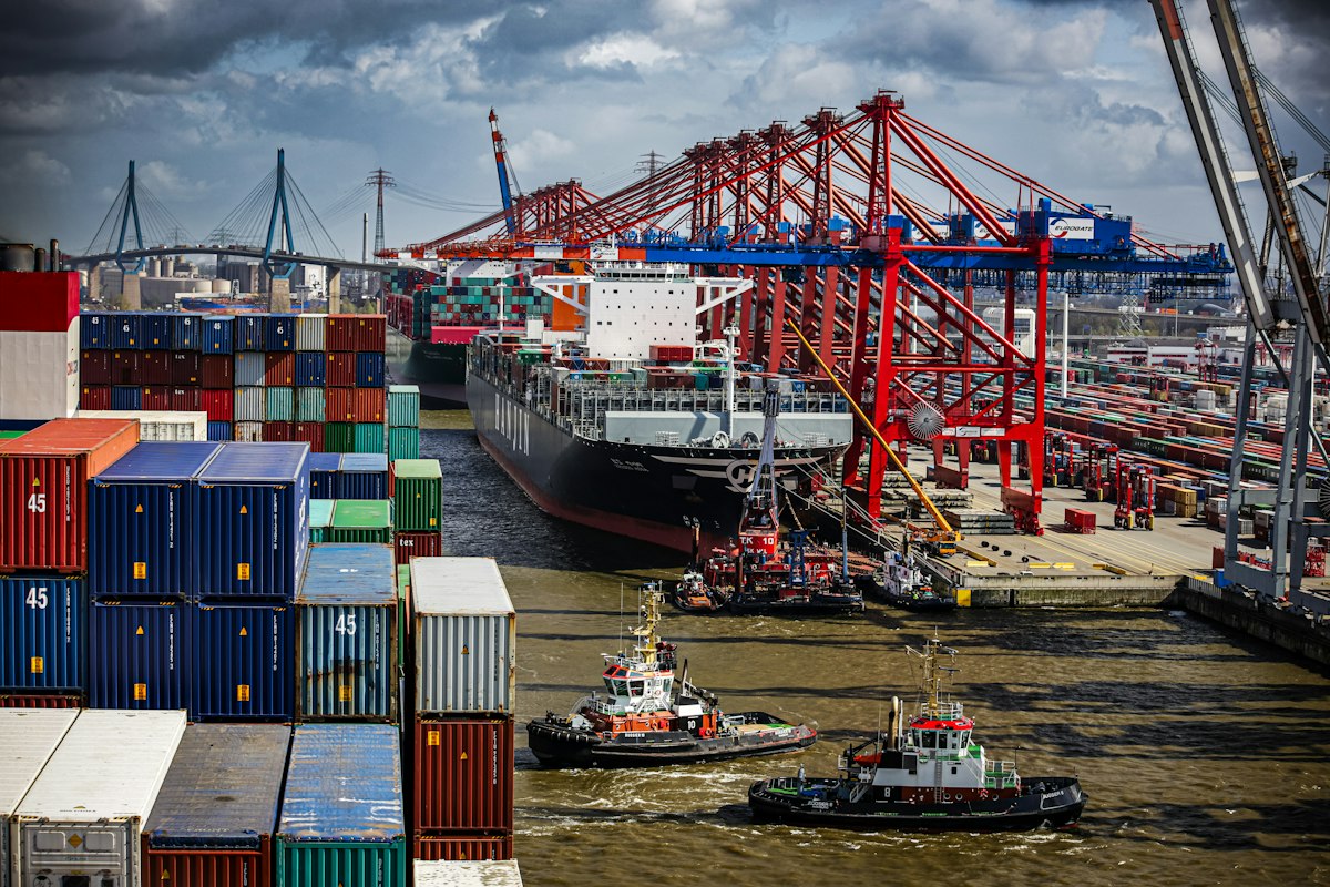Cargo ship near port cranes with tugboats alongside